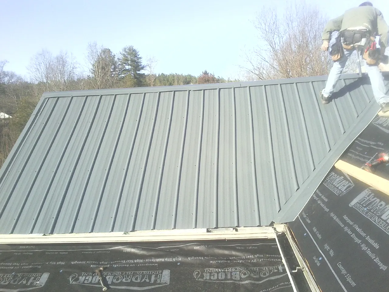Crew installing dark green standing seam panels over synthetic underlayment in New Cumberland