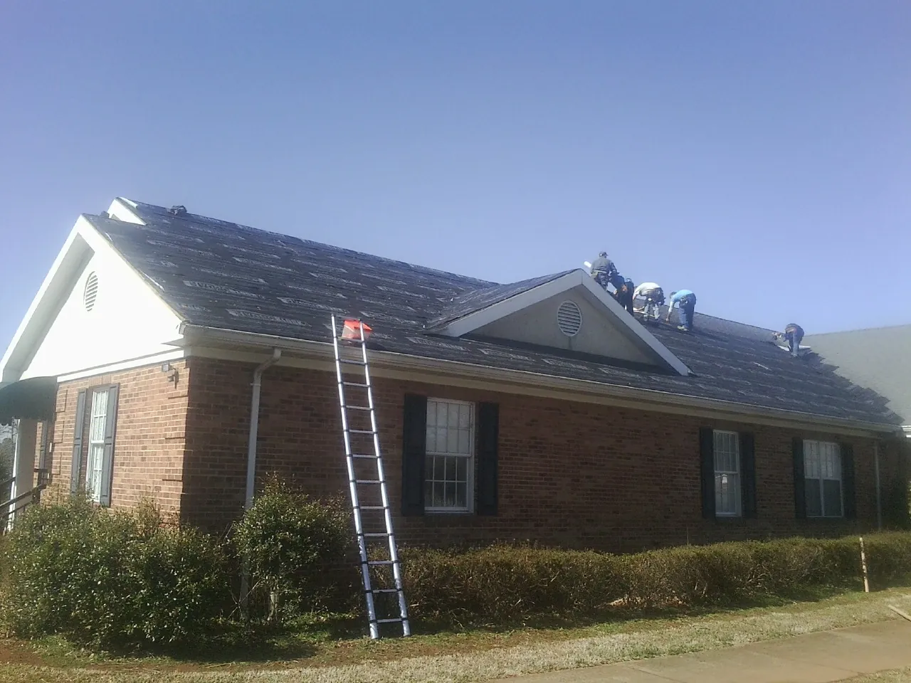 Crew tearing shingles off a brick ranch roof with a ladder set — Metal Roof Repair work by our crew in New Cumberland