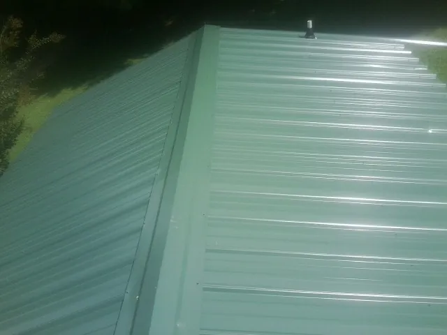 New green metal panels meeting at the ridge of a roof — Flat Roof Repair work by our crew in New Cumberland